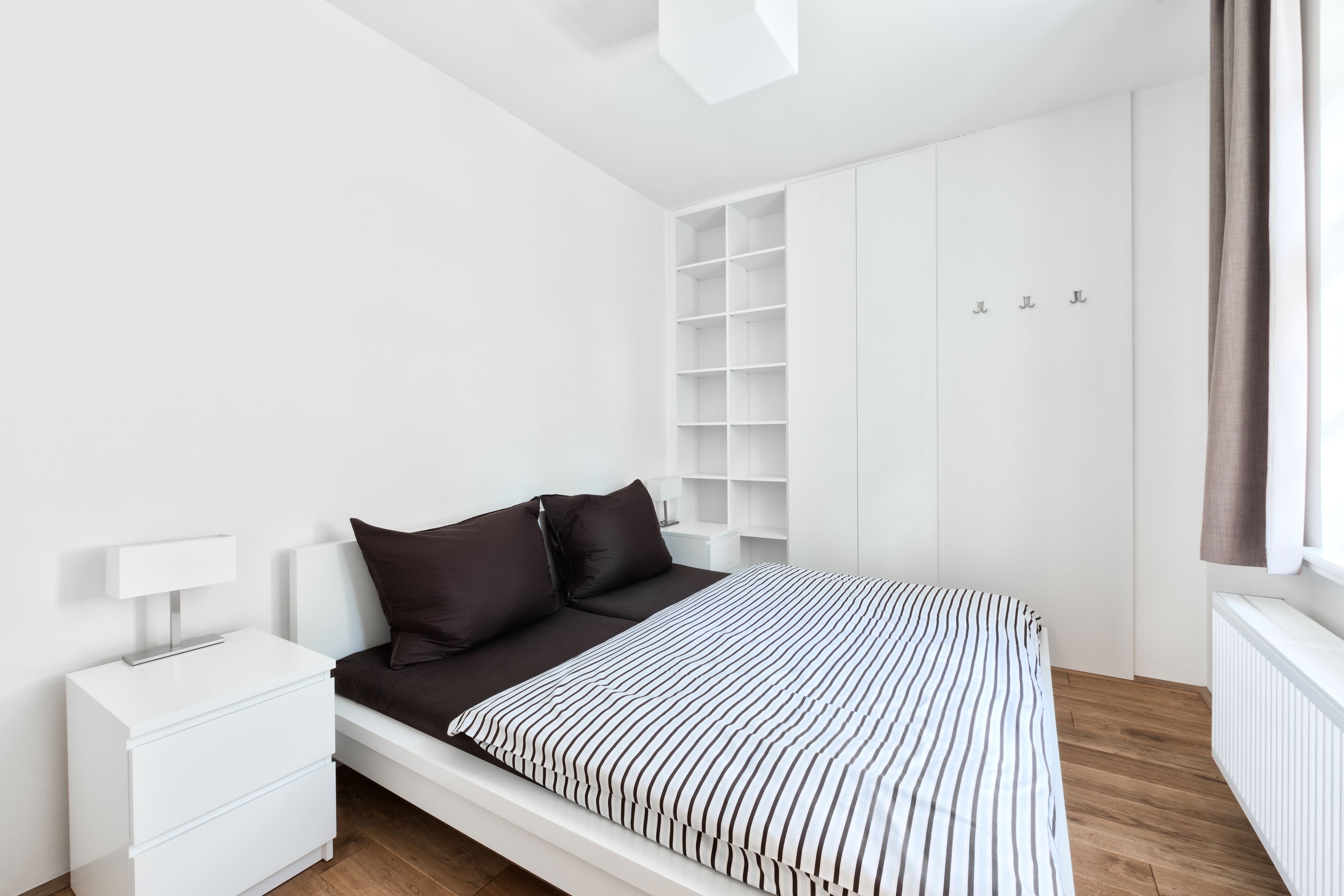 Un dormitorio moderno con cama, mesita de noche blanca y estanterías empotradas.