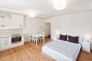 Een moderne, minimalistische slaapkamer met een groot bed, een kleine kitchenette en een eethoek.