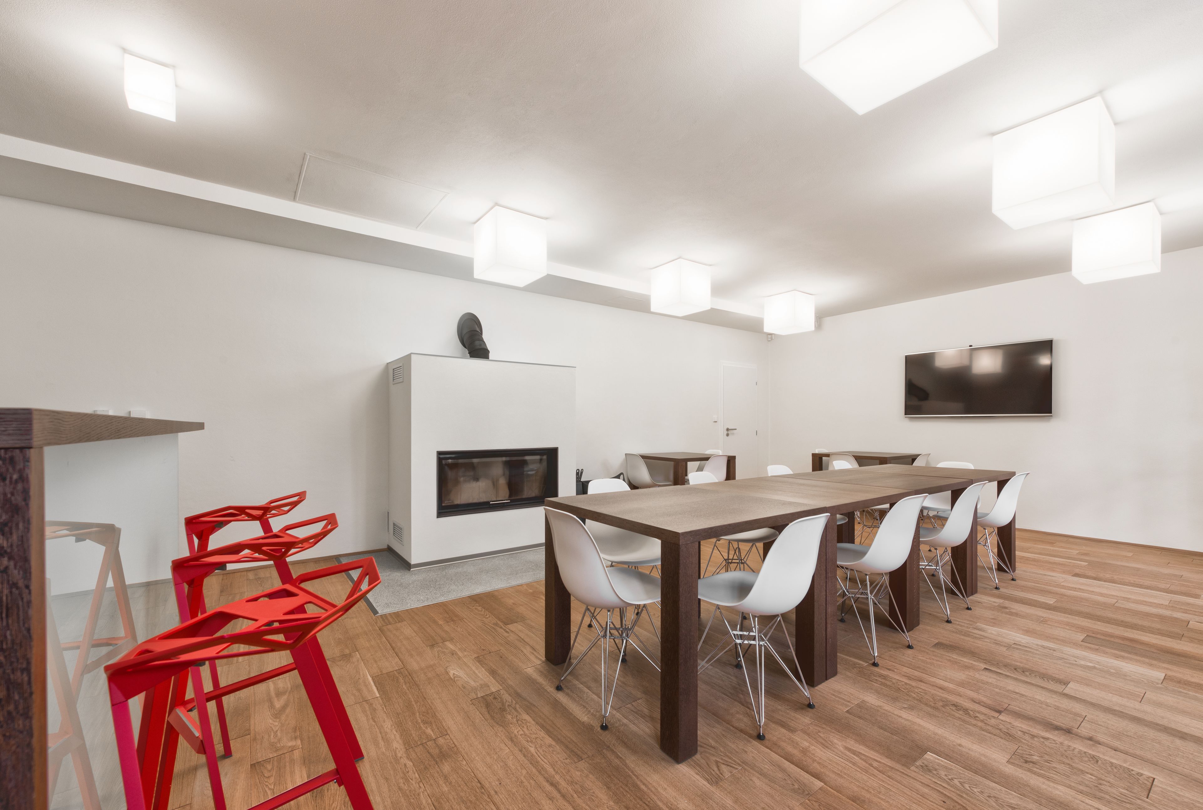 Une salle de réunion moderne avec une table en bois, des chaises blanches, une cheminée et des spots encastrés au plafond.