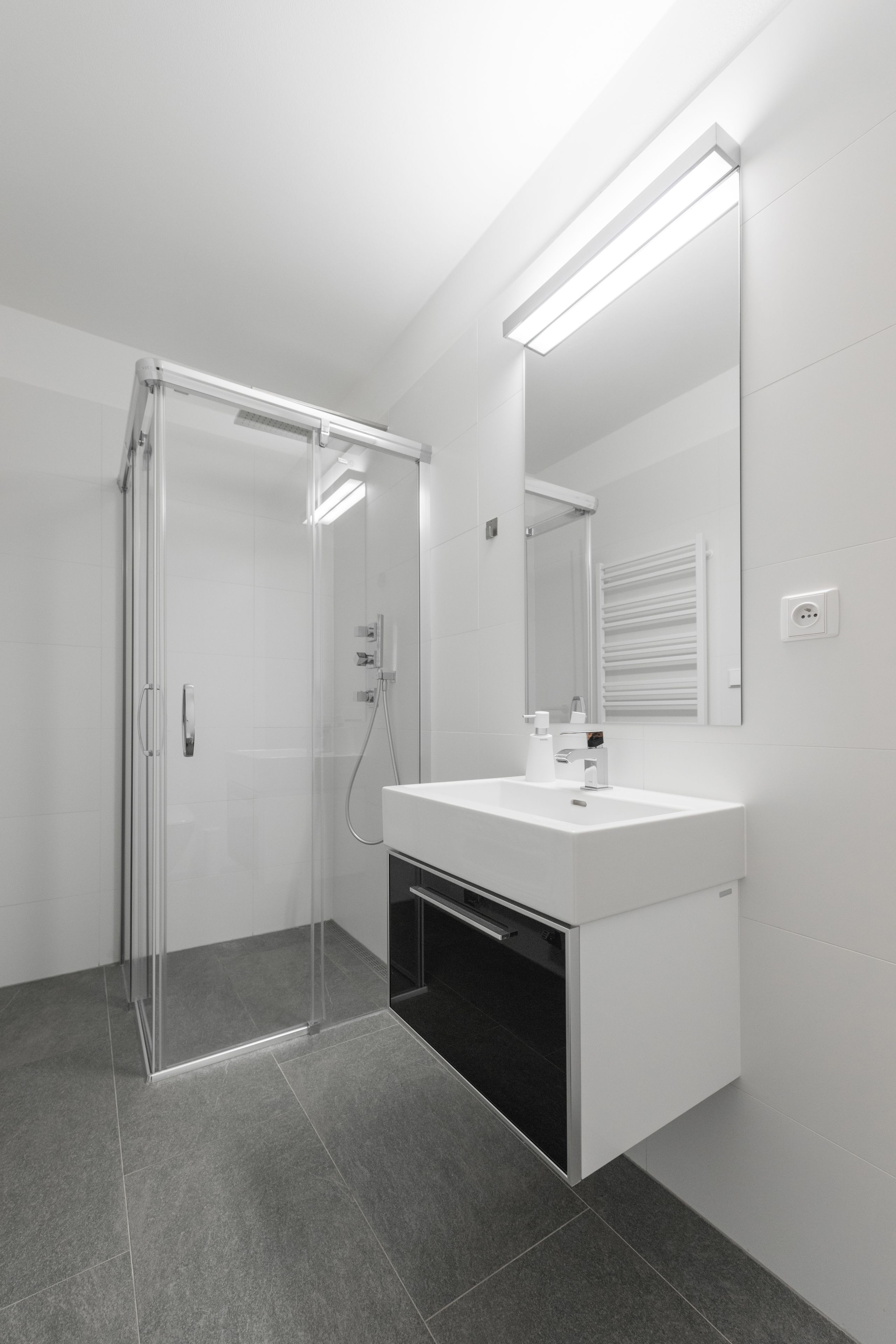 A modern bathroom with a glass shower enclosure, a white sink with a mirror, and a built-in cabinet.