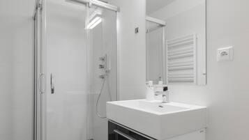 A modern bathroom with a glass shower enclosure, a white sink with a mirror, and a built-in cabinet.