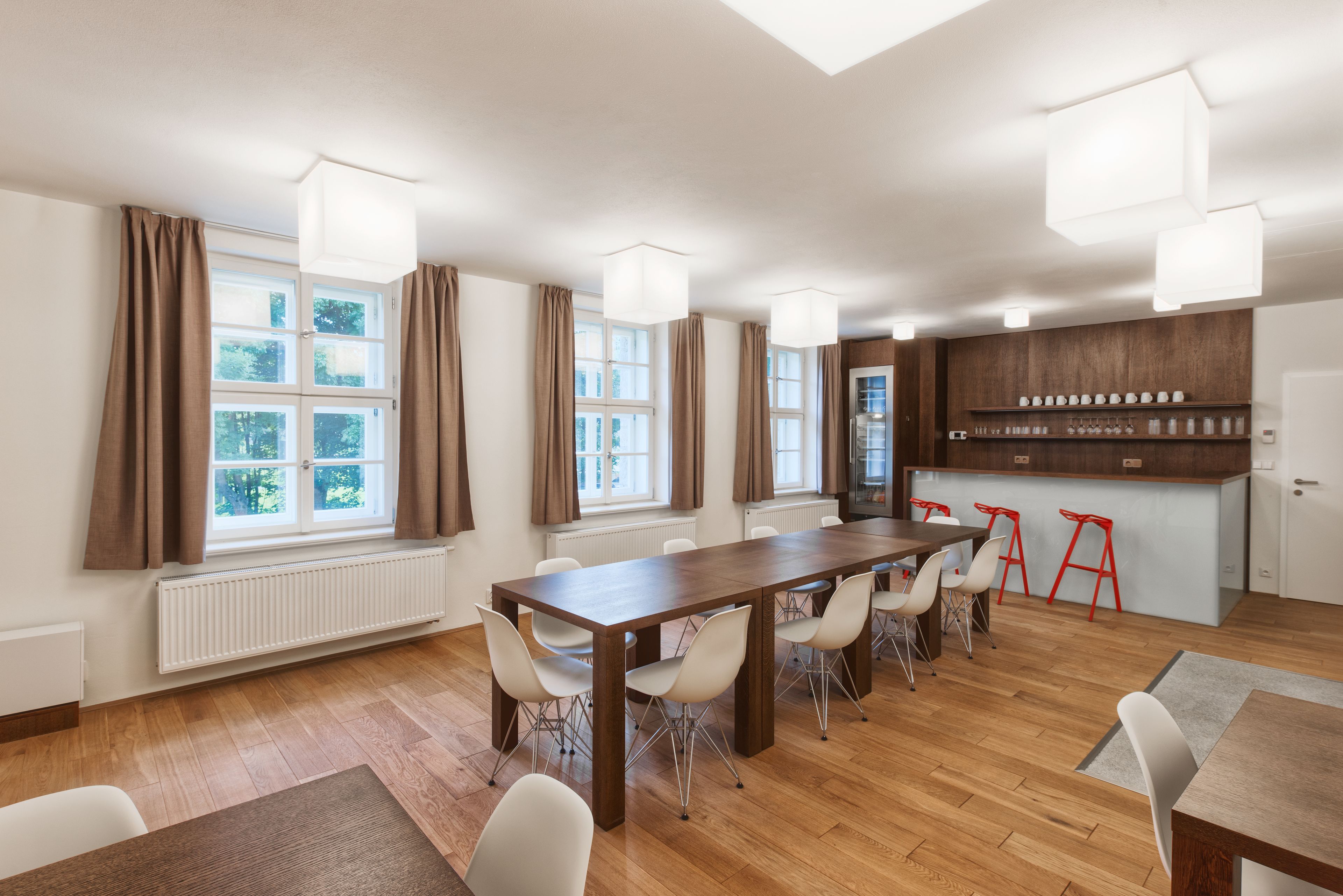 A spacious room with a long wooden table, white chairs, and a kitchen area with stools.