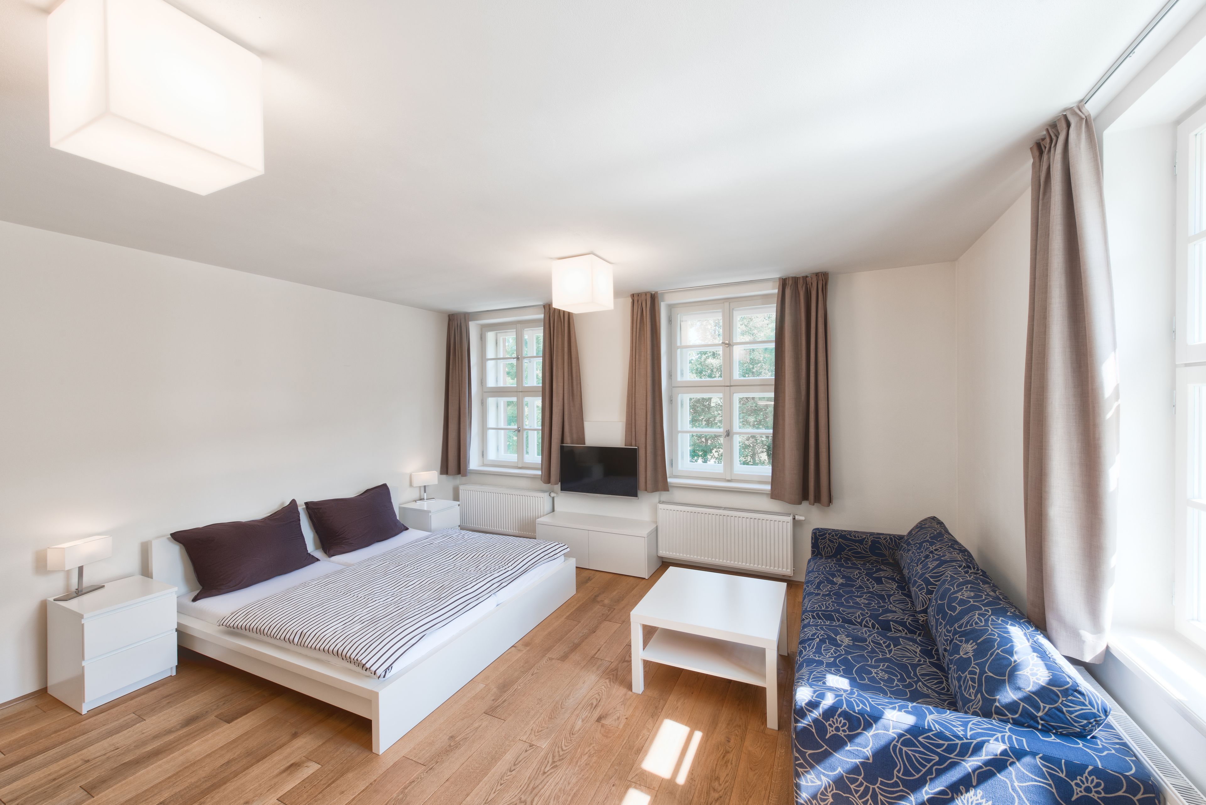 Una camera da letto moderna con un letto, comodino, televisione e un divano.