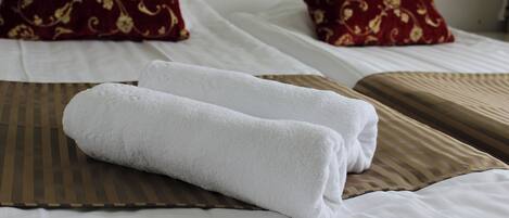 A neatly made bed with white linens and two rolled white towels.