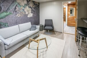 Una sala de estar moderna con un sofá gris, una mesa de centro de vidrio, una silla de madera y una pequeña mesa redonda.