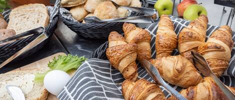 Un bufé de desayuno con pan, cruasanes y manzanas.