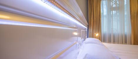 Una habitación de hotel con una cama bien hecha, un cabecero con iluminación integrada y una ventana con cortinas.