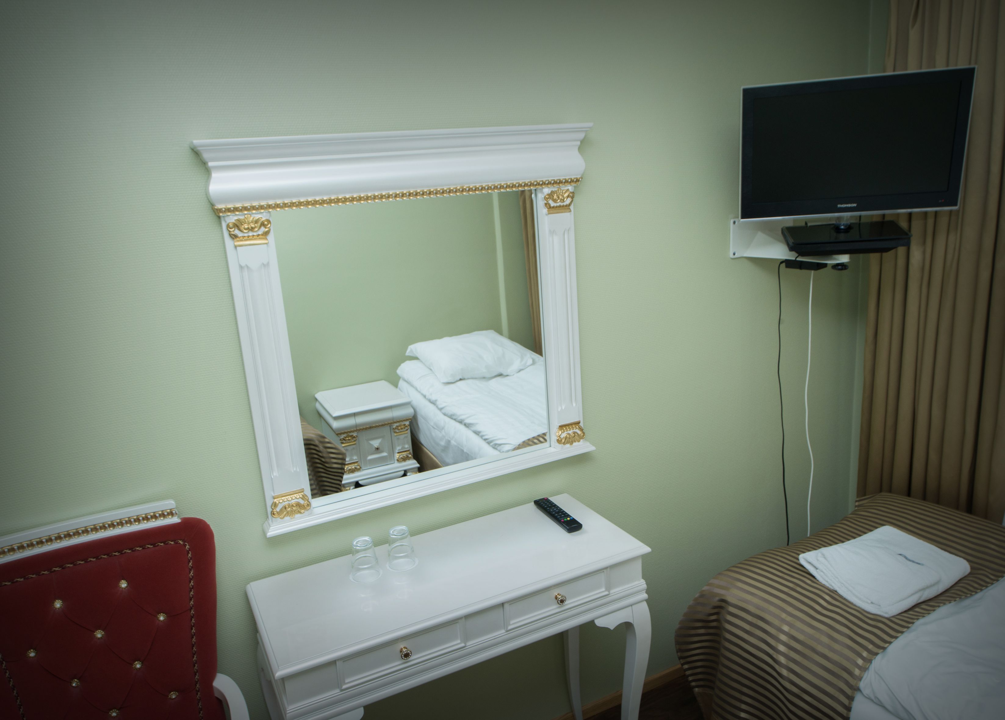 Une chambre d’hôtel avec un lit, une table de chevet avec une télécommande, un miroir et un téléviseur posé sur un meuble.
