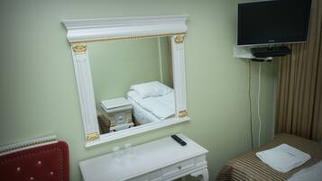 Une chambre d’hôtel avec un lit, une table de chevet avec une télécommande, un miroir et un téléviseur posé sur un meuble.