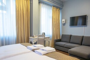 Una habitación de hotel con cama, sofá, escritorio con silla, televisor y cortinas.