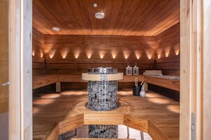 Una sauna con paredes y bancos de madera, una estructura central de piedra e iluminación en el techo.