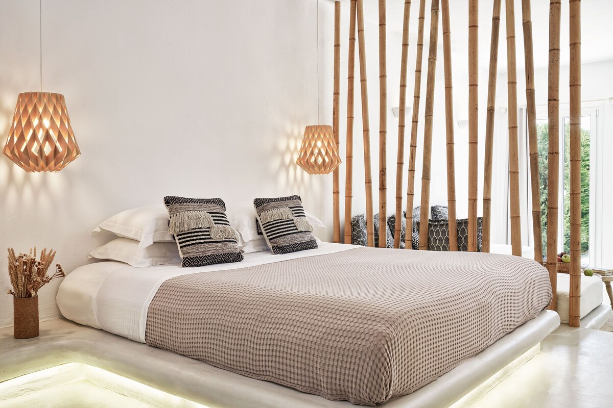 Una cama bien tendida con colcha a cuadros, dos almohadas estampadas y dos lámparas colgantes de diseño geométrico.