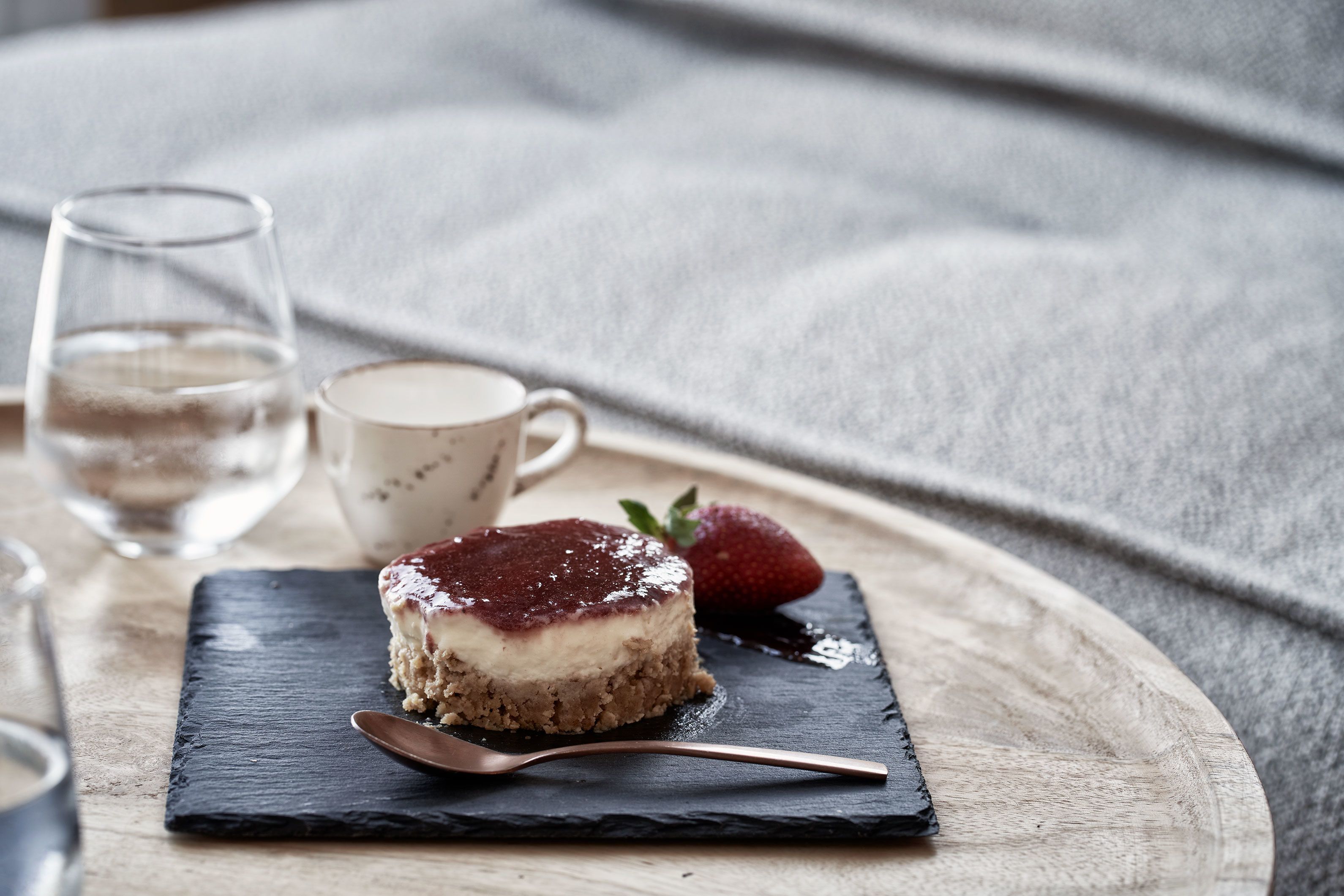 Un postre sobre una fuente de pizarra con una cuchara, un vaso de agua y una taza al fondo.