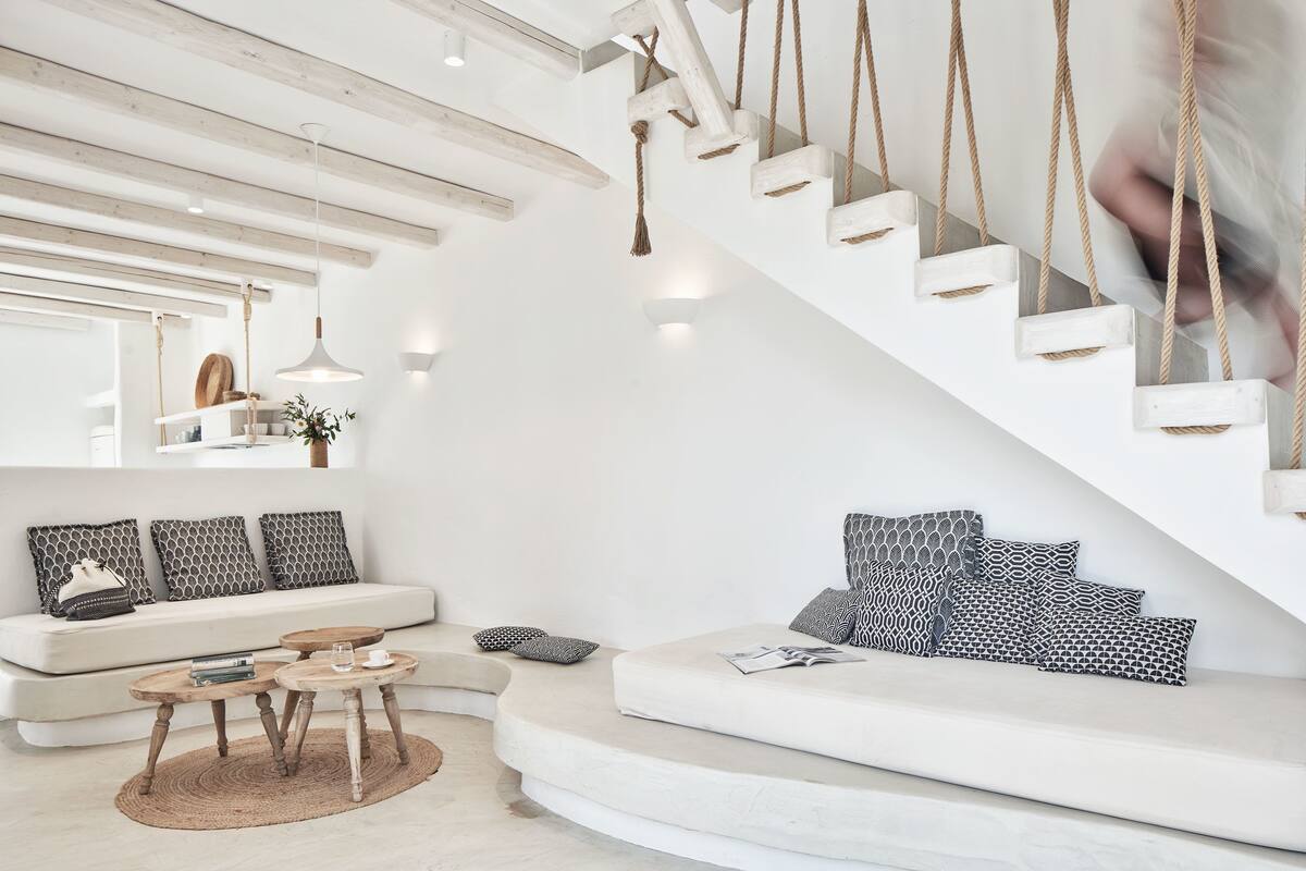 Una sala de estar moderna con un sofá blanco, una mesa de centro redonda y una escalera con escalones de madera y barandillas de cuerda.