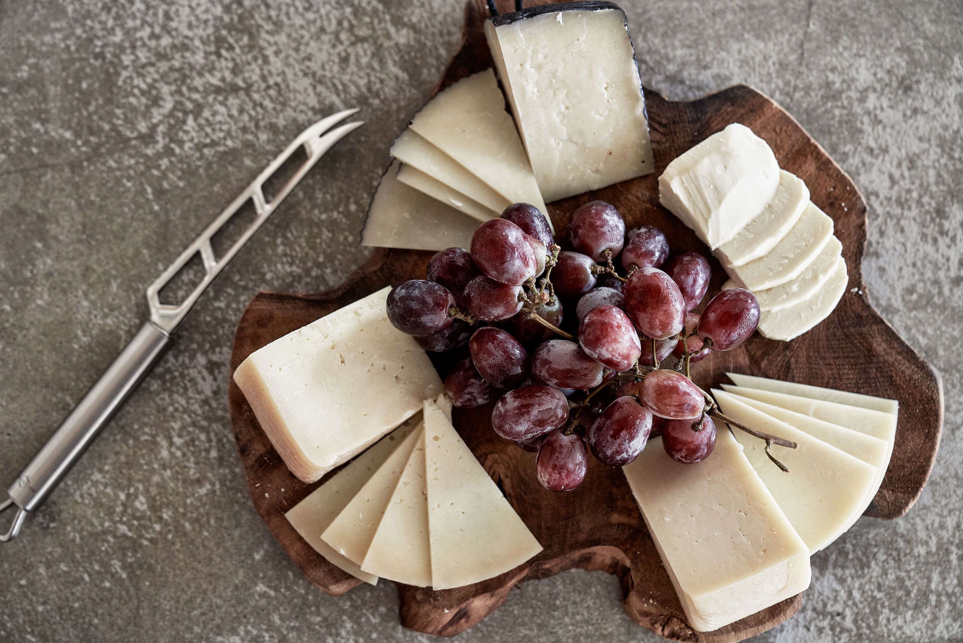 Un tagliere con diverse fette di formaggio e un grappolo d'uva.