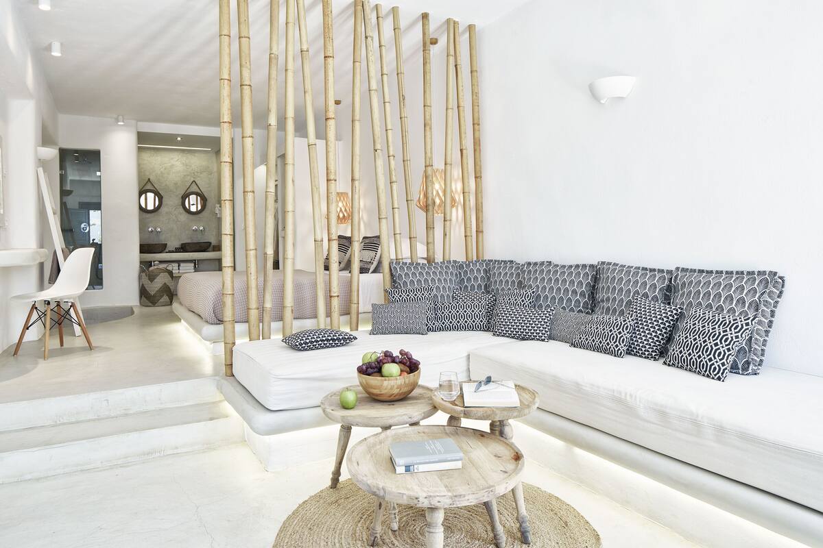 Una sala de estar moderna con un sofá blanco, cojines estampados, una mesa de centro de madera con un cuenco de frutas y una mampara de bambú.