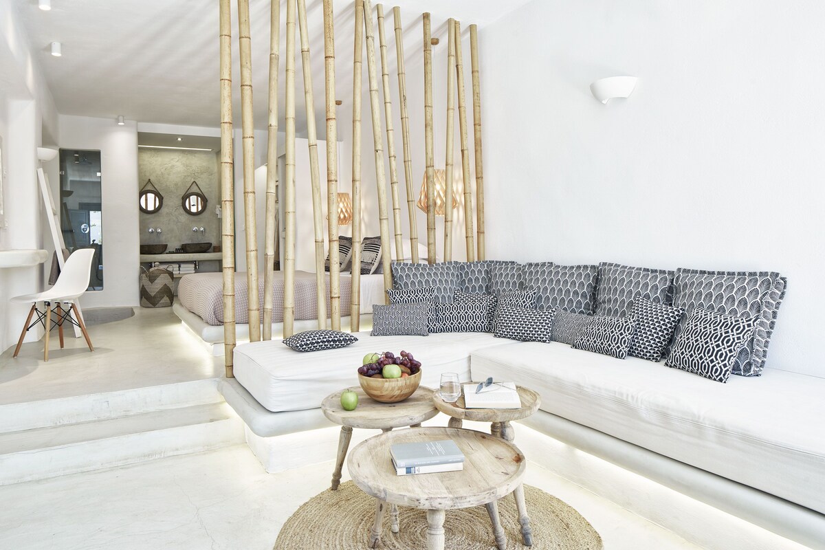 Un salon moderne avec un canapé blanc, des coussins à motifs, une table basse en bois sur laquelle se trouve un saladier rempli de fruits, et un paravent en bambou.