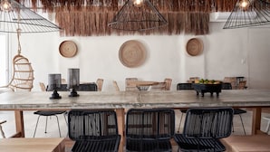A dining area with a concrete table, black woven chairs, and a thatched ceiling. - Naxian Utopia Luxury Villas & Suites (Naxos)