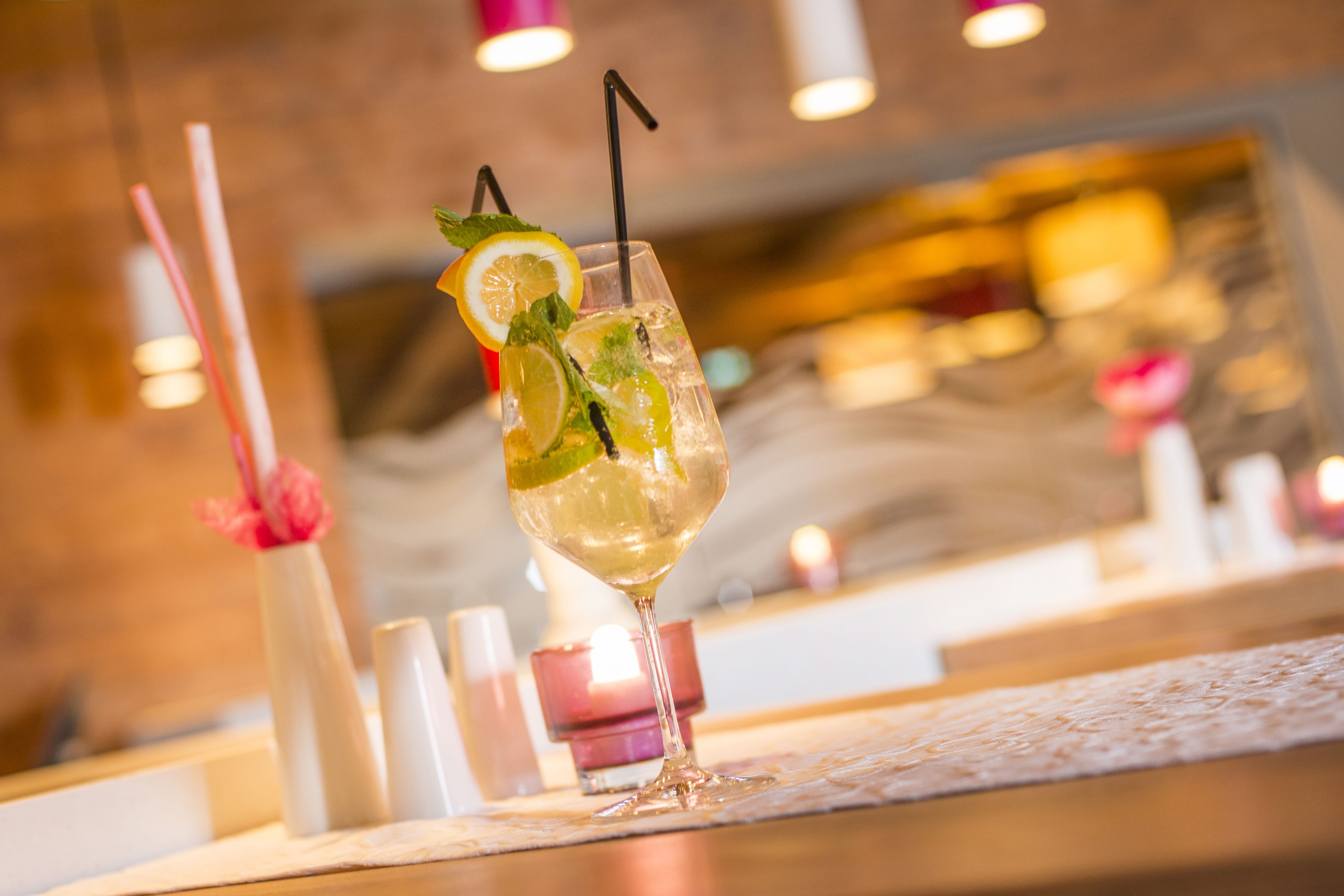 A cocktail glass with a lemon slice and mint garnish on a bar counter.