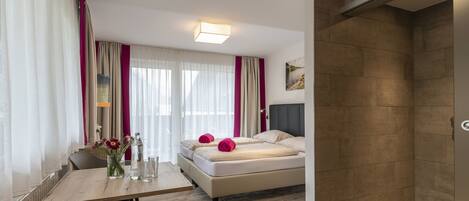 Una habitación de hotel moderna con una cama, un escritorio con una silla, una zona de ducha y una ventana con cortinas.