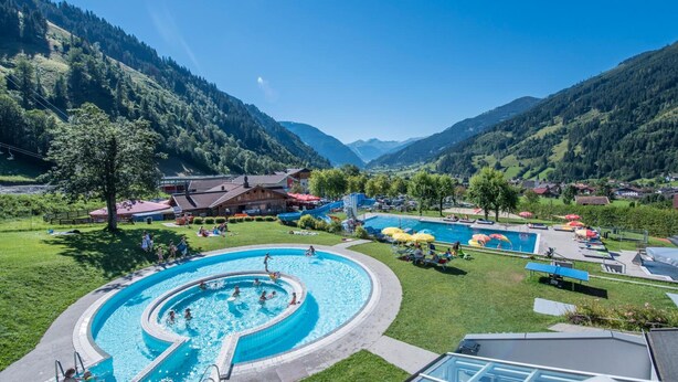 A swimming pool surrounded by a lush green landscape and mountains. - smartHOTEL (Dorfgastein)