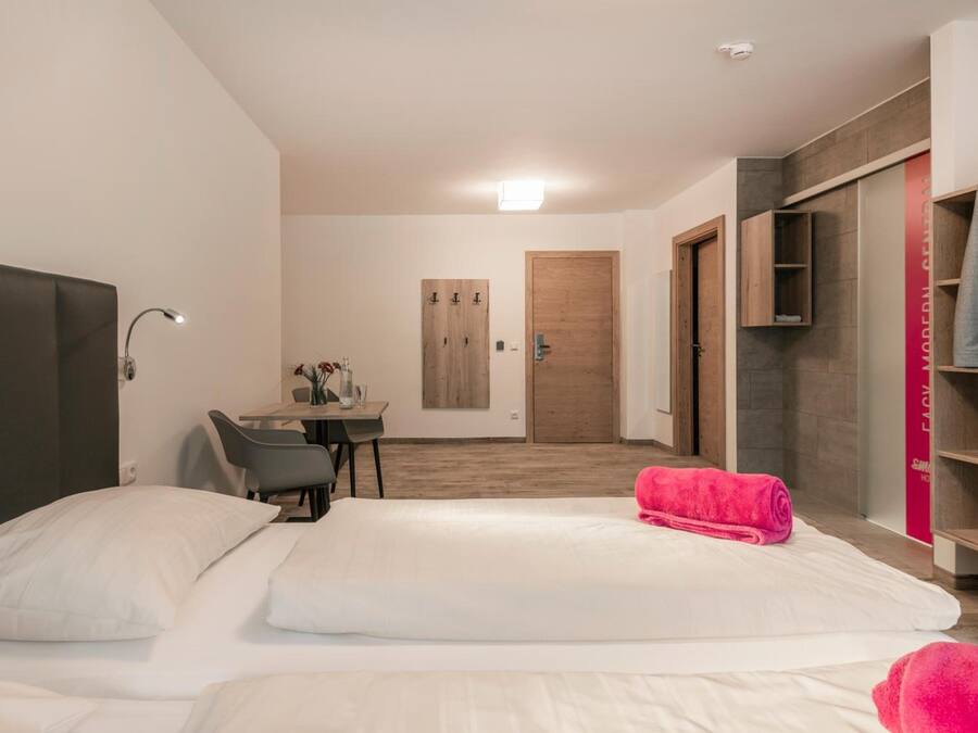 A hotel room with two beds, a desk, a chair, and a TV.