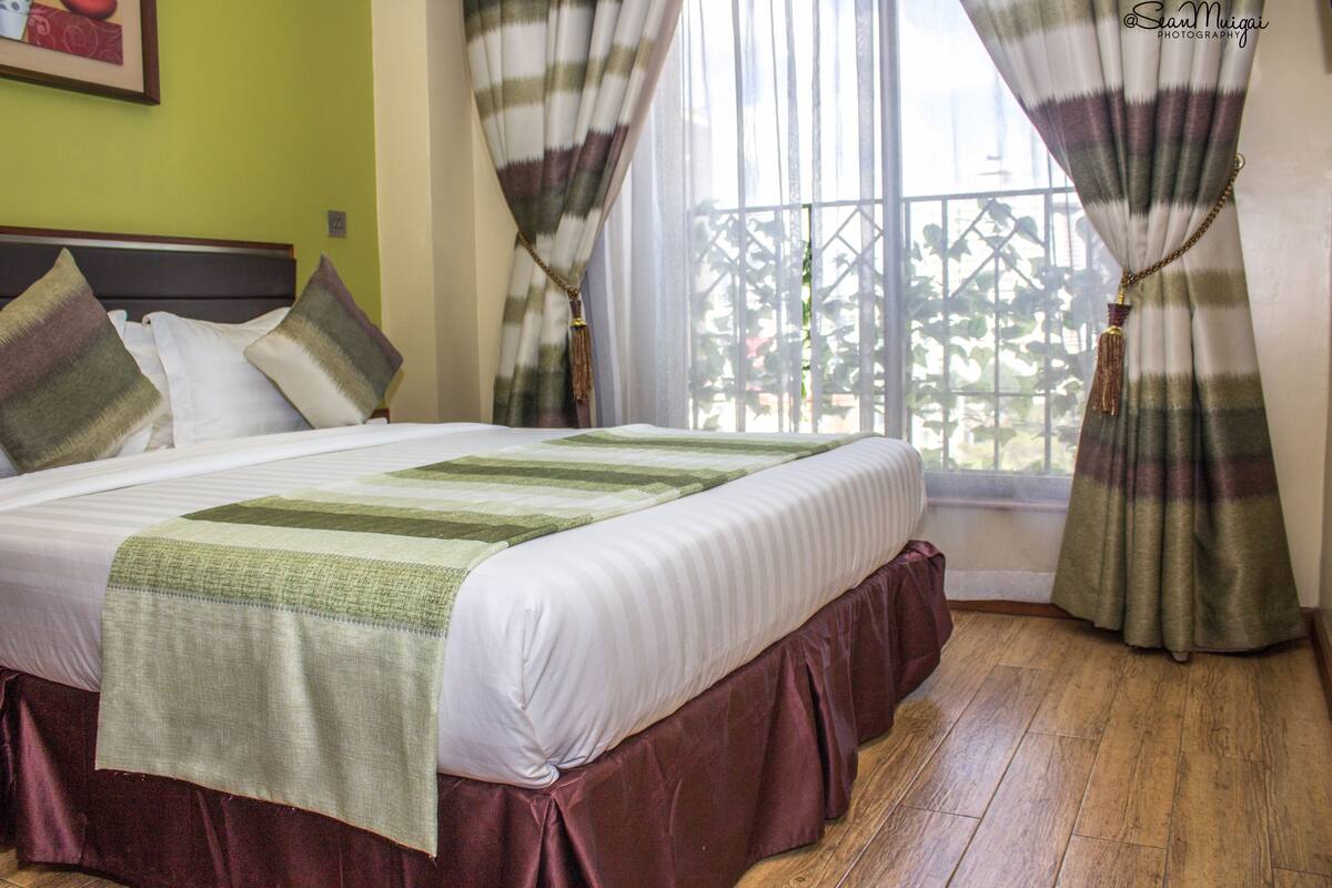 A neatly made bed with a green and white striped bedspread, a wooden headboard, and a view of a balcony with a metal railing.