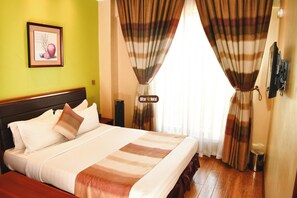 A hotel room with a bed, curtains, a framed picture, and a trash bin. - After 40 Hotel (Nairobi)
