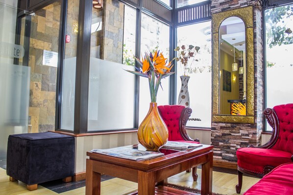 A lobby with a stone wall, a large mirror, red upholstered chairs, a wooden coffee table, and a vase with flowers. - After 40 Hotel (Nairobi)