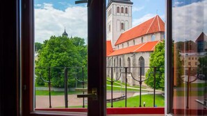 Uitzicht vanuit een raam met balkon, uitkijkend op een kerk met een rood dak en een hoge toren.