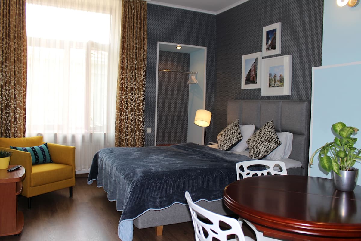 Ein Hotelzimmer mit einem Bett, einem gelben Sessel, einem Esstisch und einer Zimmerpflanze.