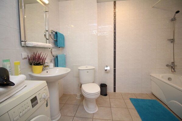 A bathroom with a white sink, toilet, and bathtub. There is a blue bath mat on the floor, and a potted plant on the sink.