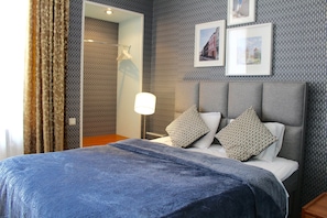 A hotel room with a bed, a nightstand, a lamp, and a wall with patterned wallpaper and framed pictures. - Tallinn City Apartments Harju Residence (Tallinn)