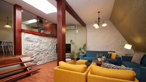 Een moderne woonkamer met een blauwe bank, gele fauteuils en een houten trap.