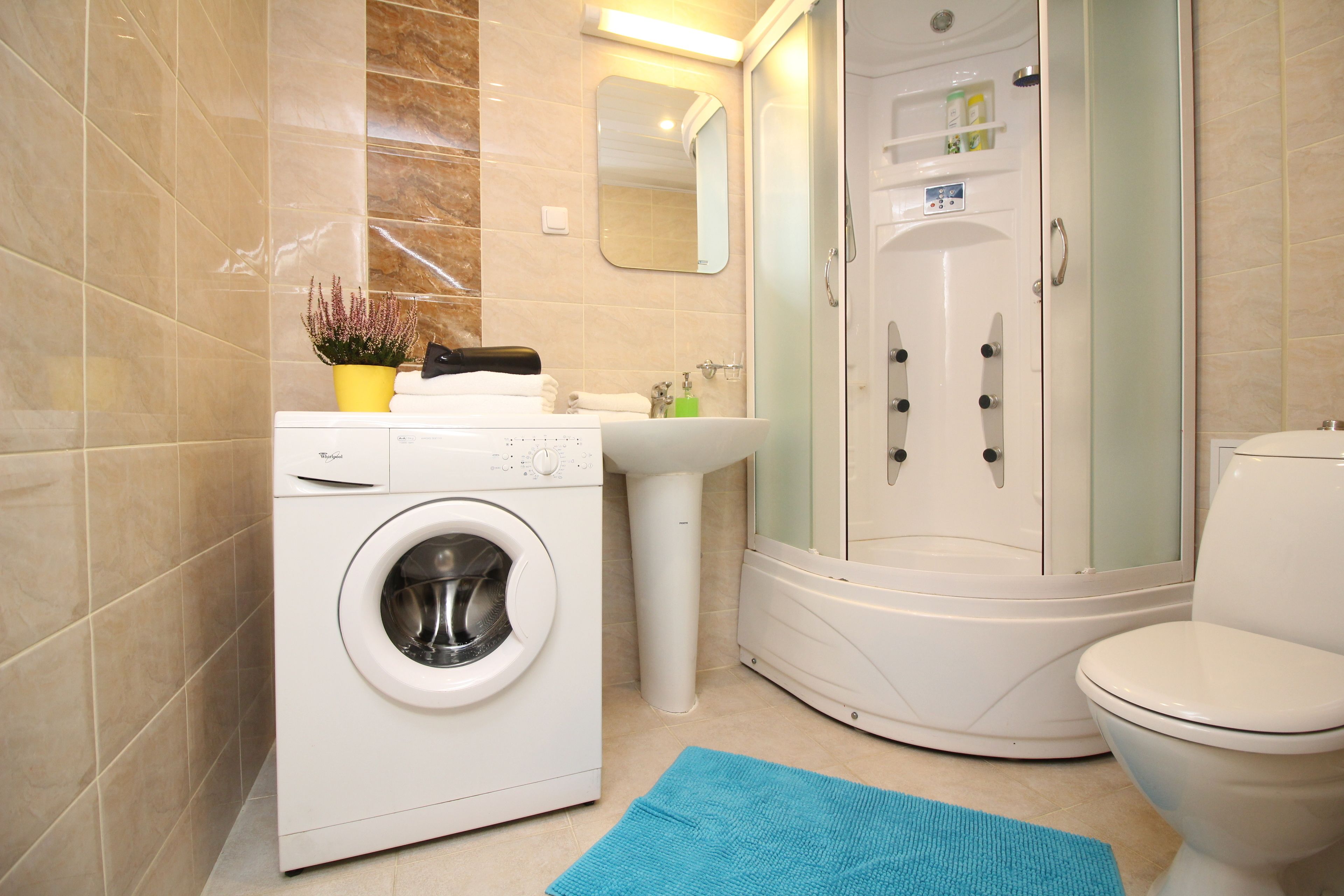 A modern bathroom with a washing machine, a sink, a toilet, and a glass-enclosed shower.