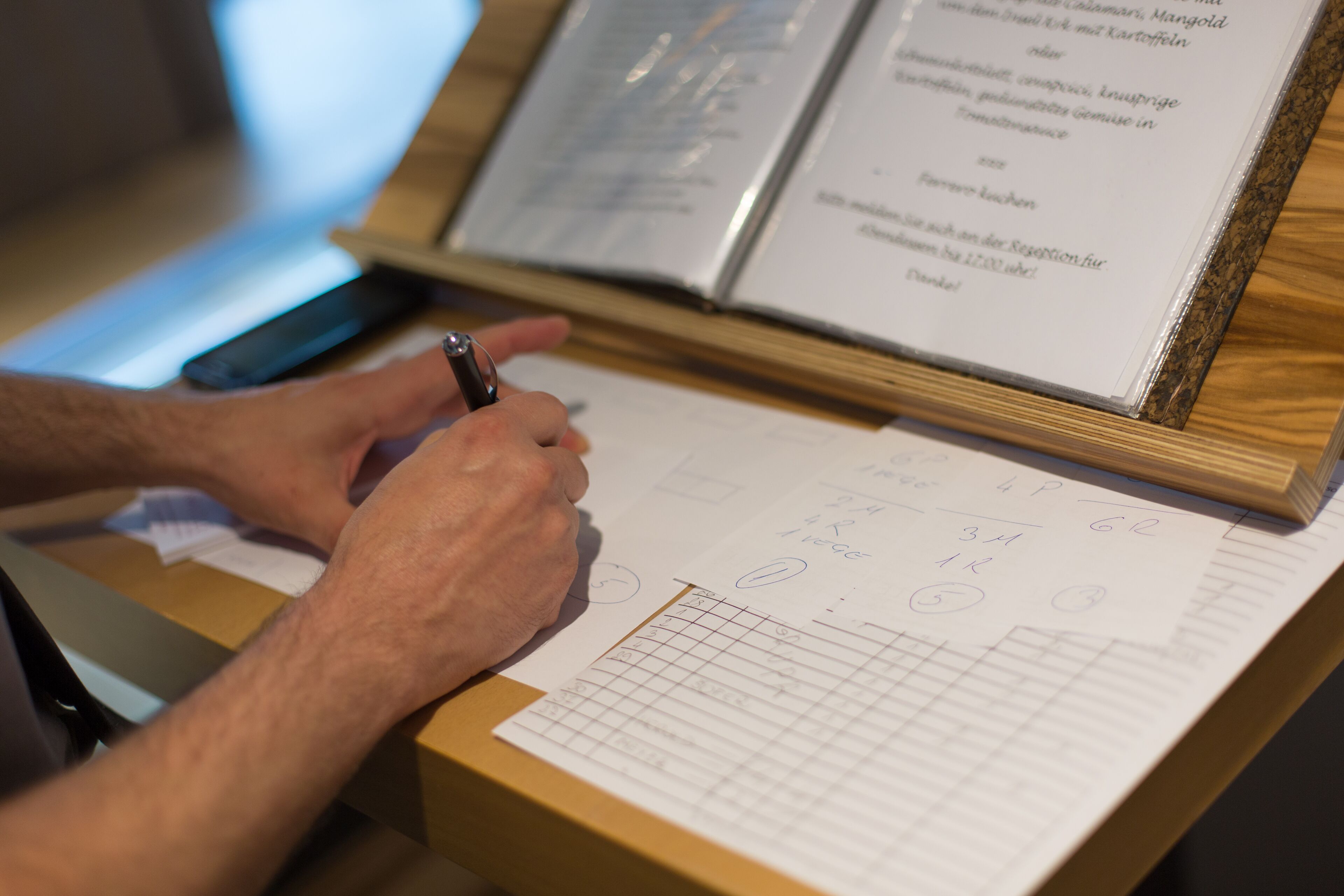 A person writing on a clipboard with a pen, surrounded by papers with handwritten notes and diagrams.