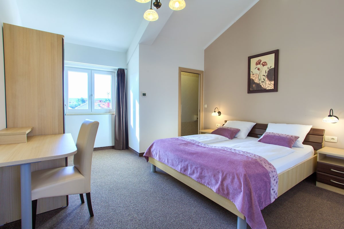 Ein Hotelzimmer mit Bett, Schreibtisch, Stuhl, Fenster und Tür.