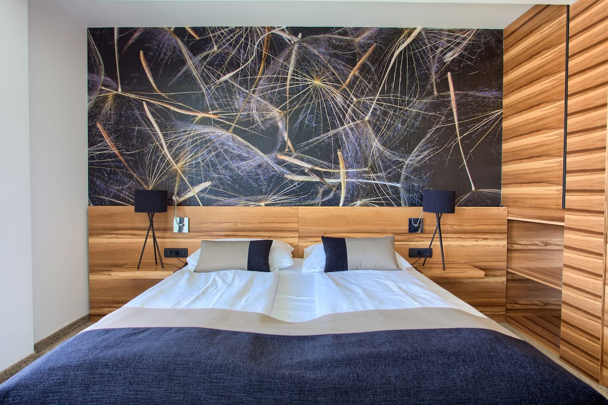 Ein modernes Schlafzimmer mit einem Holz-Kopfteil, einer großen abstrakten Wandkunst, zwei Nachttischen mit Lampen und einem ordentlich bezogenen Bett.