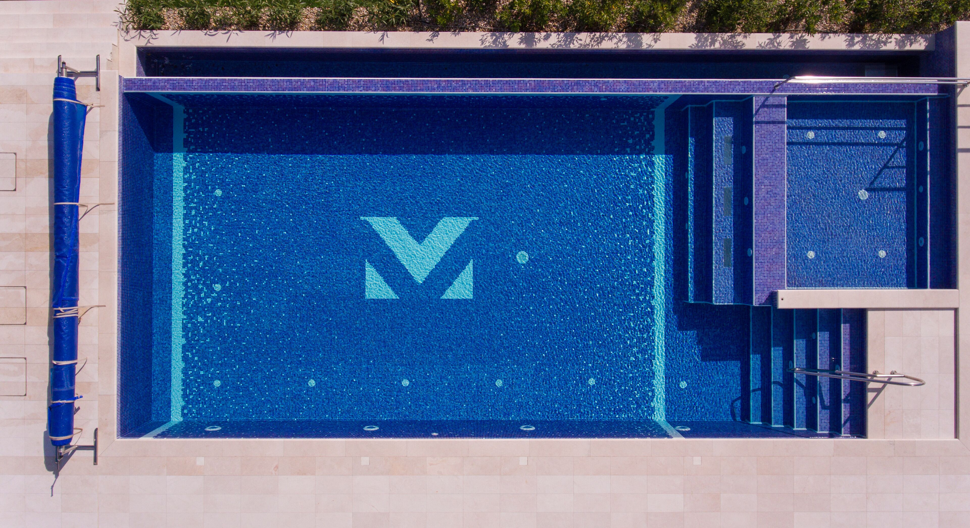 A swimming pool with a large 'V' logo, a small pool area, and a metal handrail.
