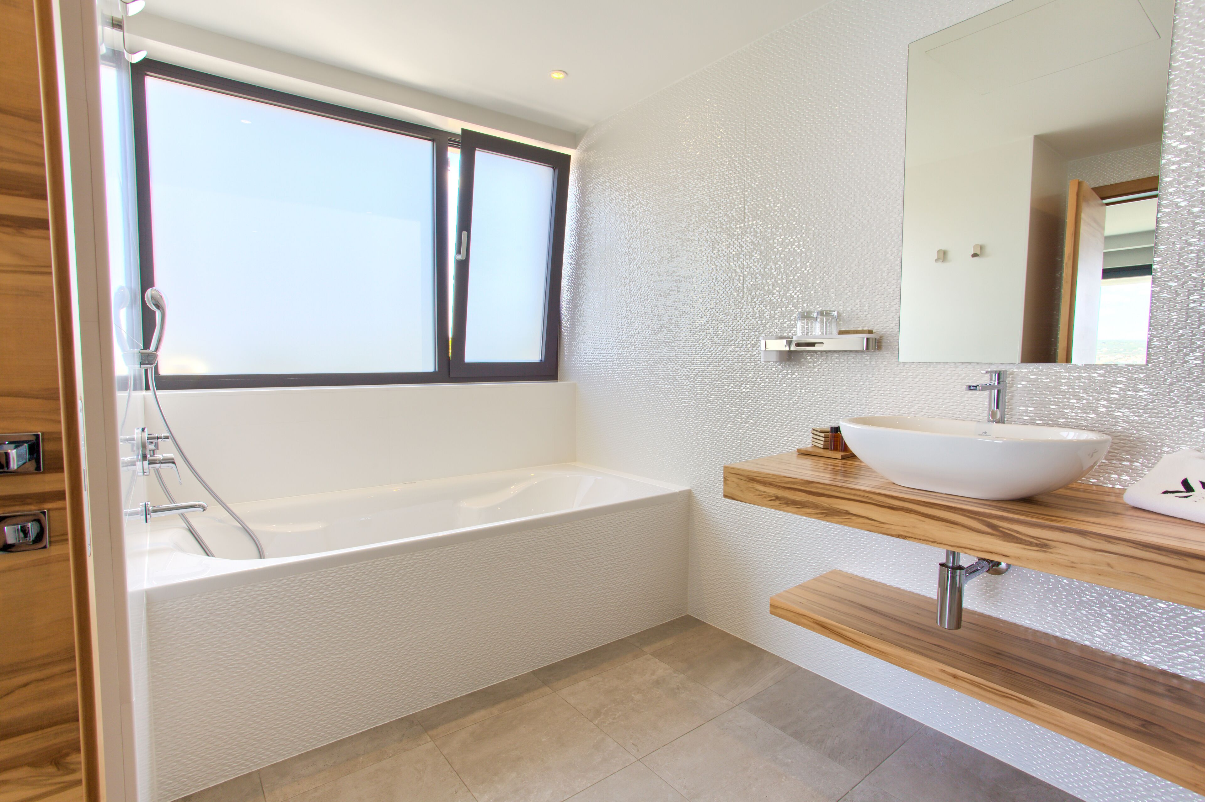 A modern bathroom with a bathtub, a large mirror, and a wooden vanity.