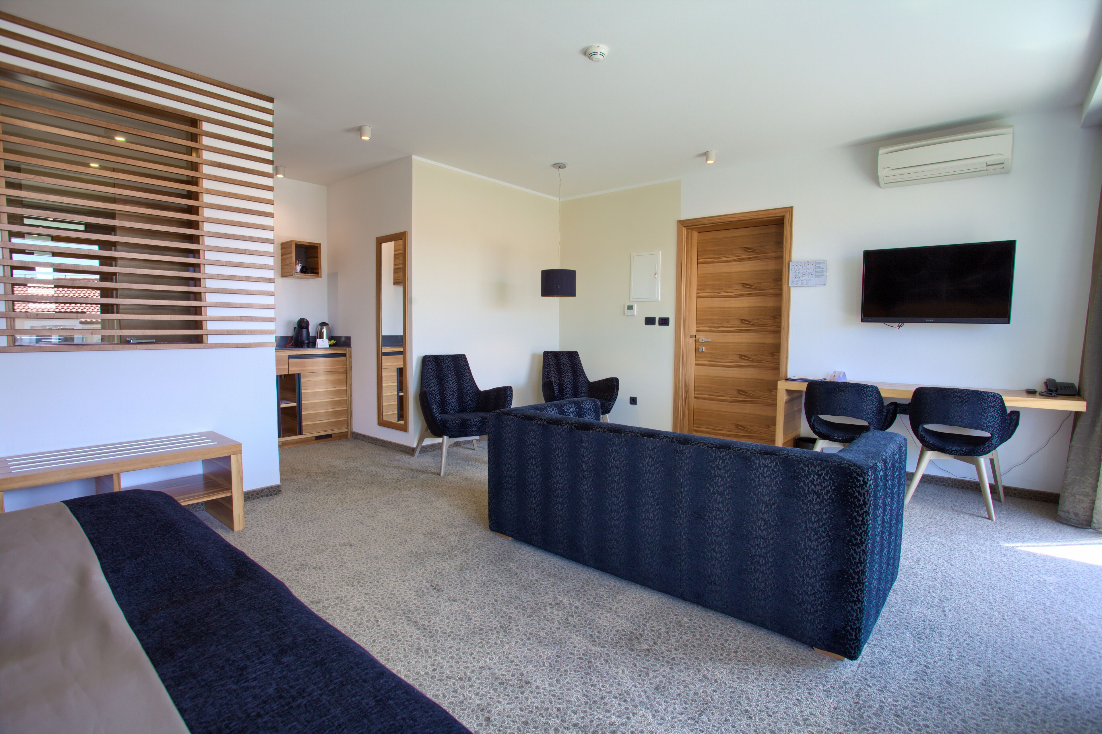 Quarto de hotel moderno com uma cama grande, área de estar com cadeiras, escrivaninha e televisão.