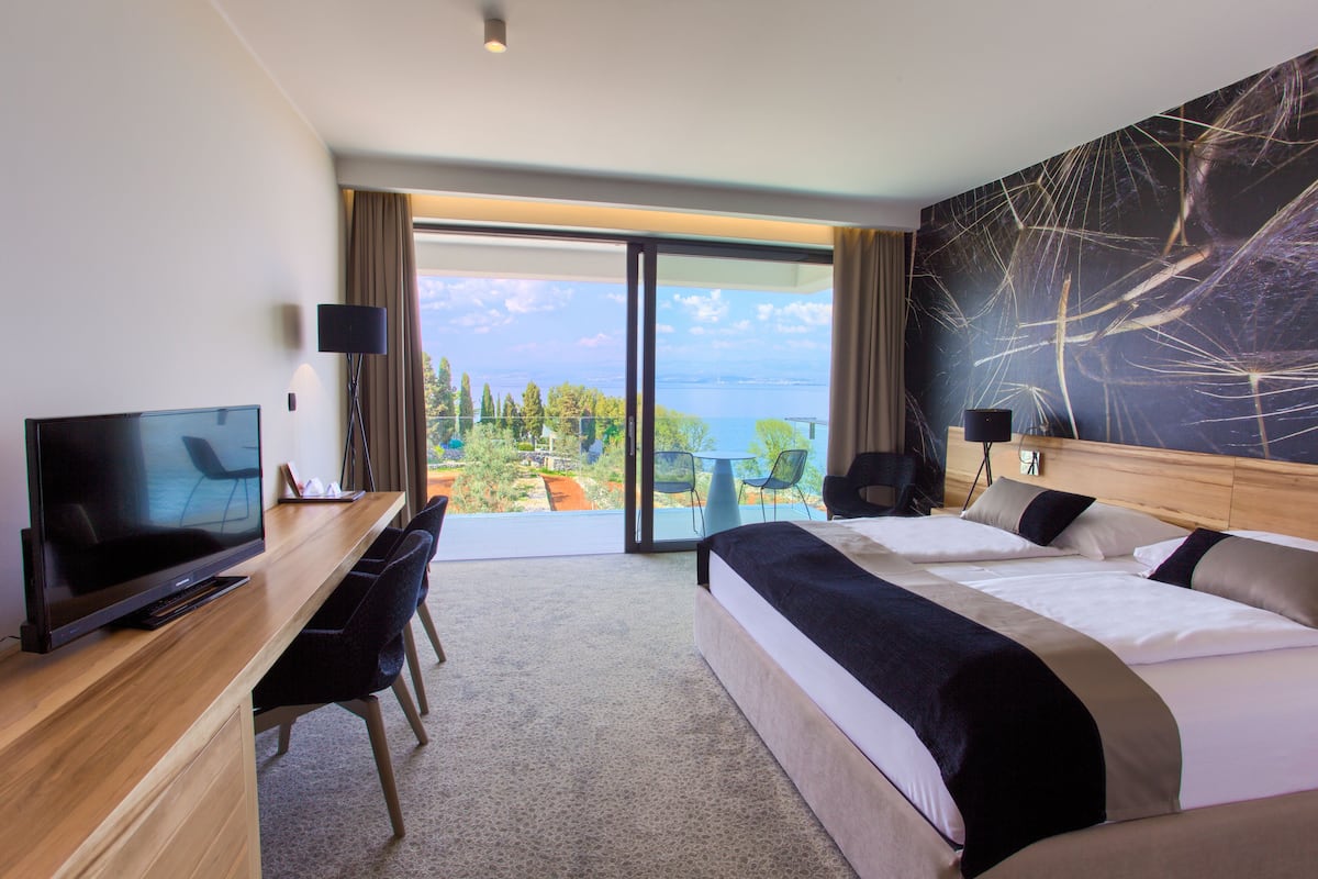 Ein Hotelzimmer mit einem großen Bett, einem Schreibtisch mit Fernseher und einem Balkon mit Meerblick.