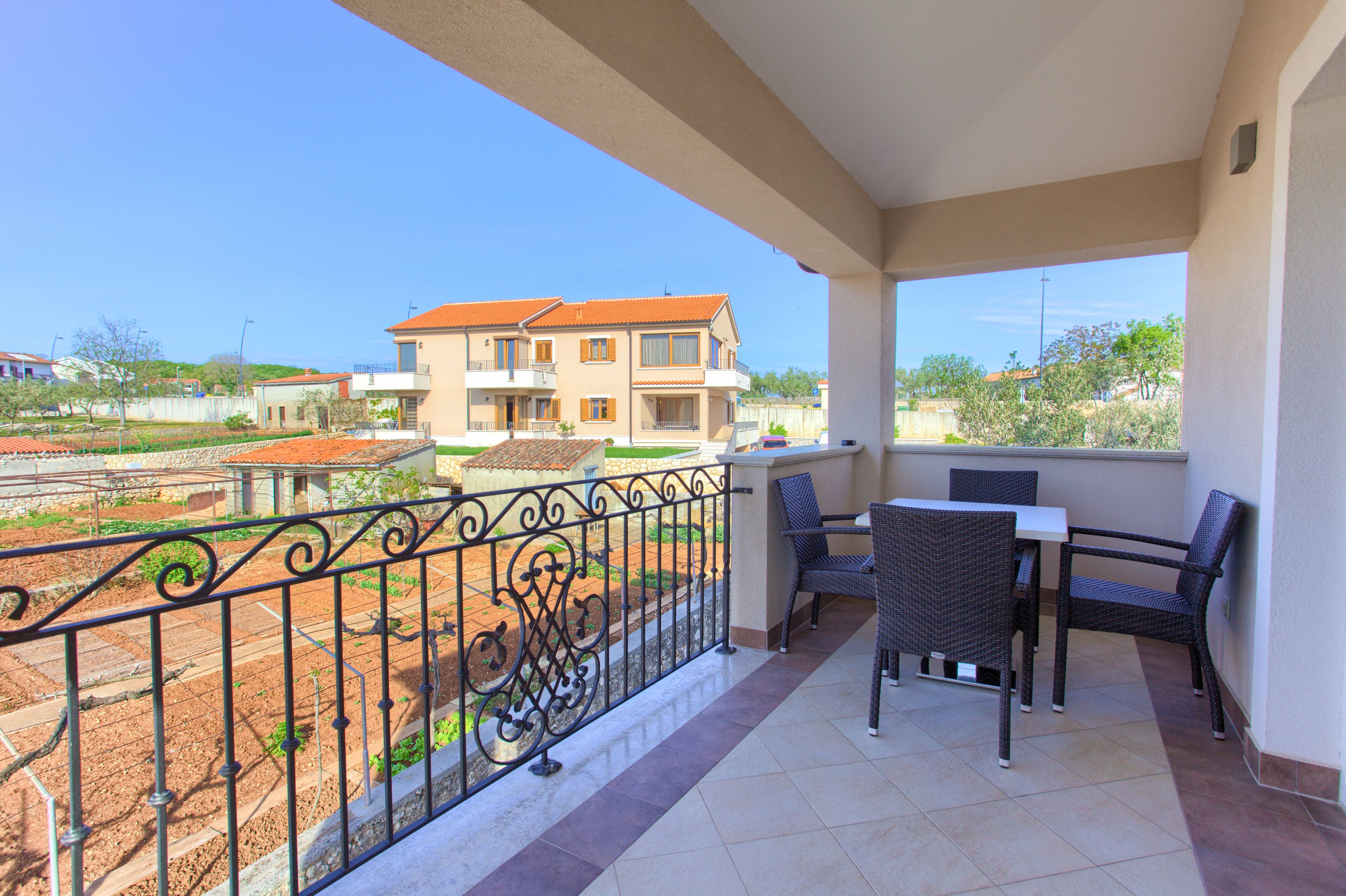 A balcony with a table and chairs, a view of a building, and a metal fence.