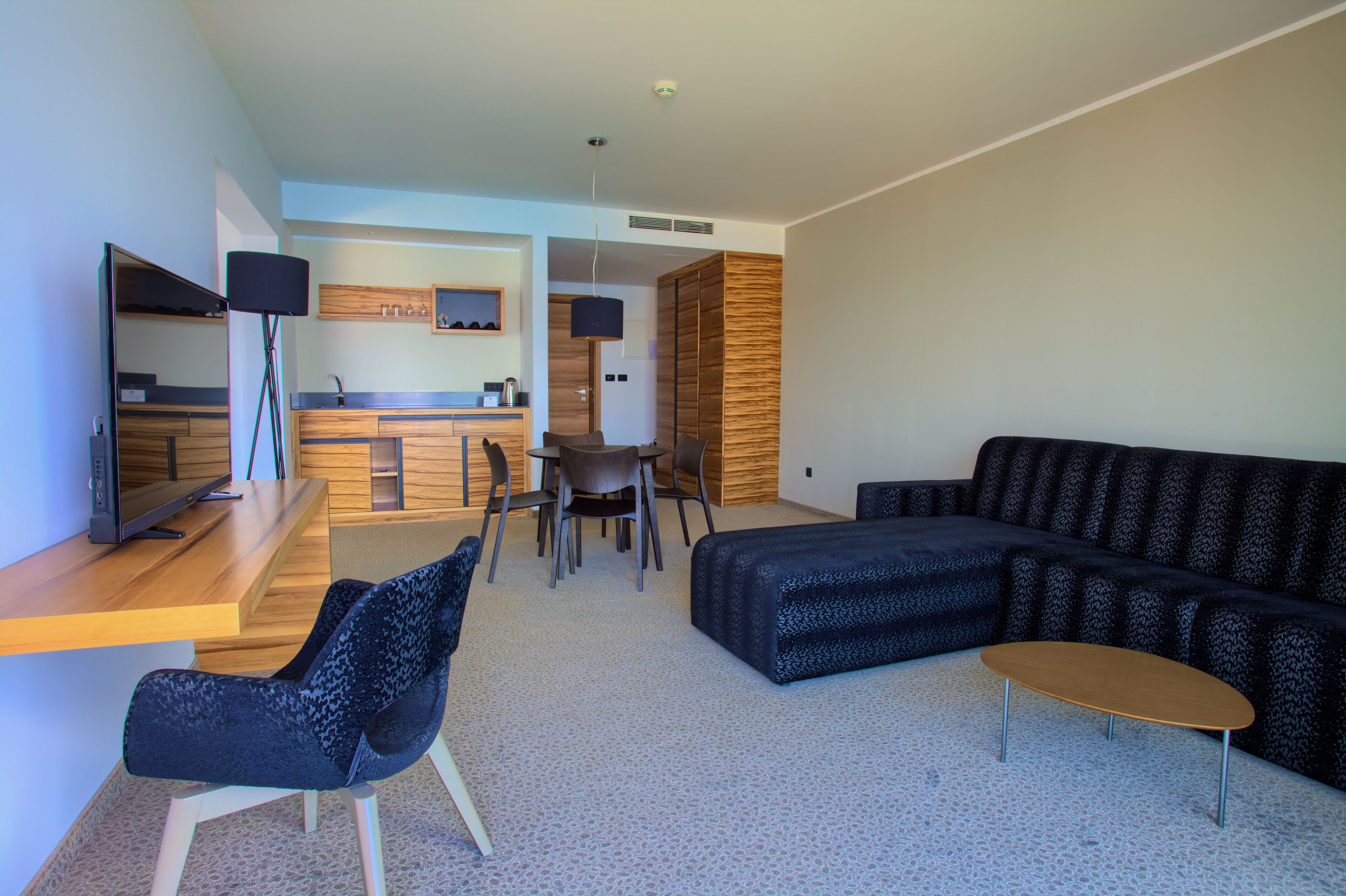 A modern living room with a sofa, a coffee table, and a TV. There is a dining area with a table and chairs.