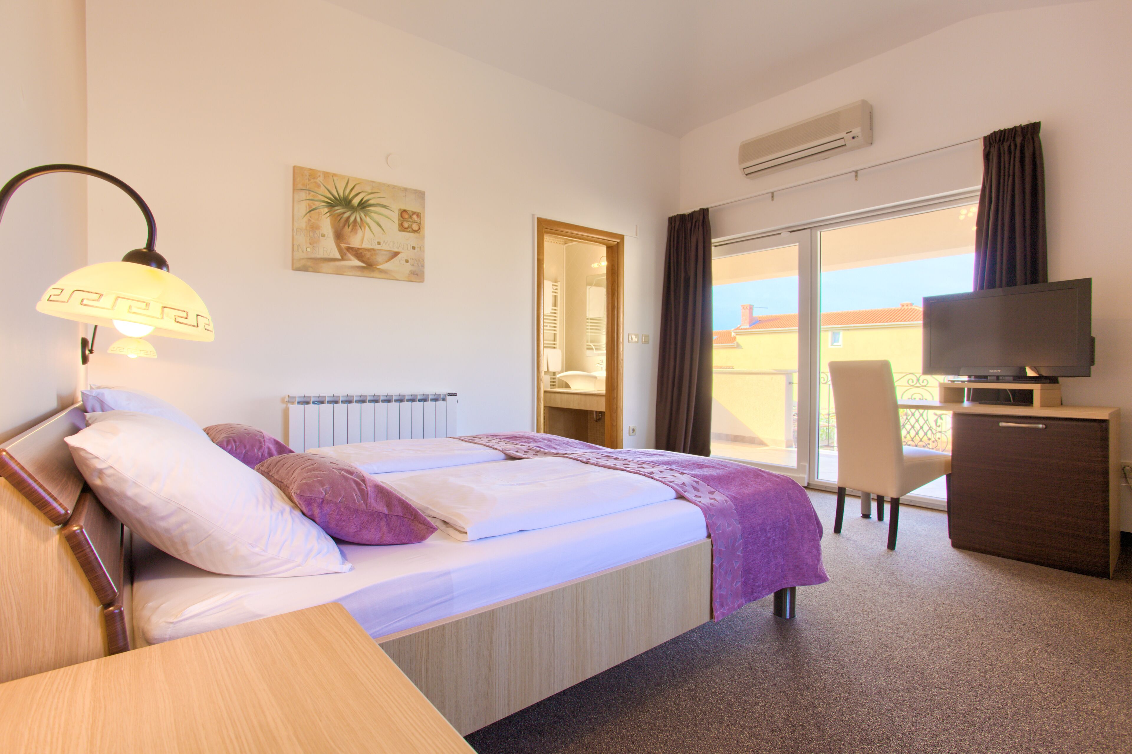 A hotel room with a bed, a desk, a television, and a balcony with a view.