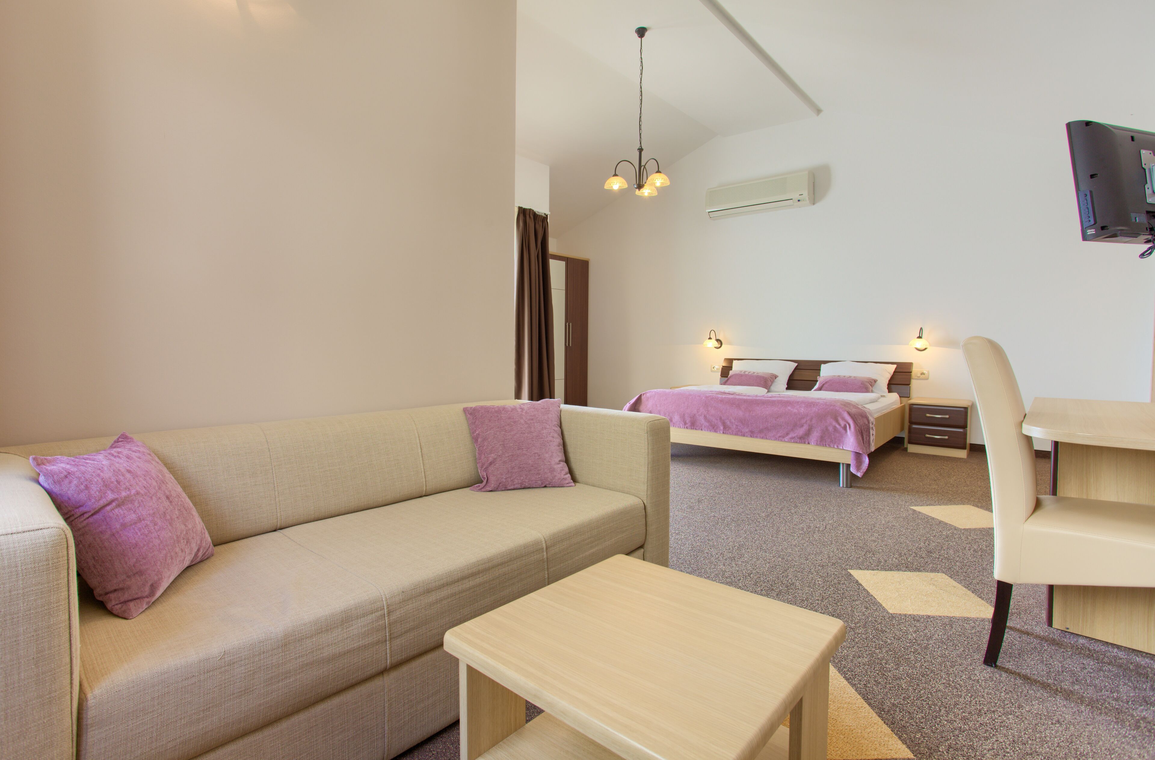 Una habitación de hotel moderna con sofá, escritorio, cama y televisor montado en la pared.