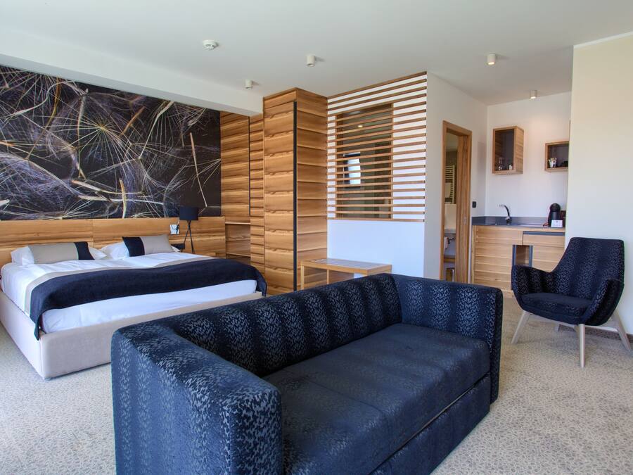 A modern hotel room with a large bed, a sofa, a desk, and a large abstract painting on the wall.