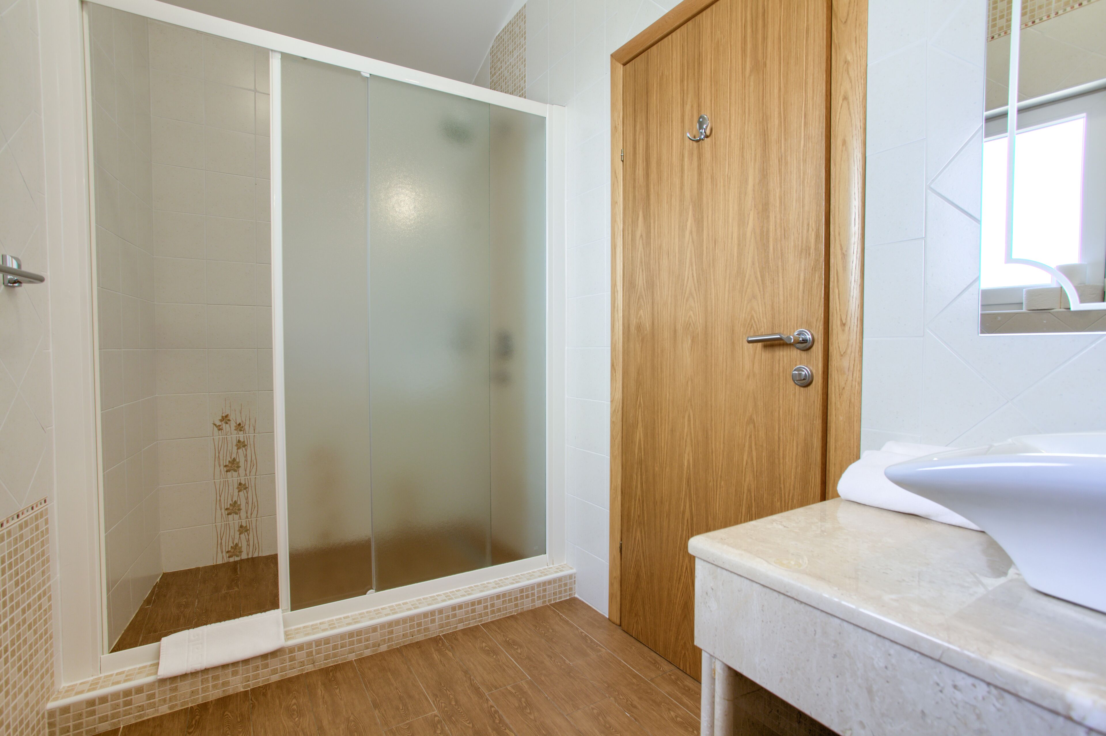 A bathroom with a wooden door, a white sink, and a glass shower enclosure.