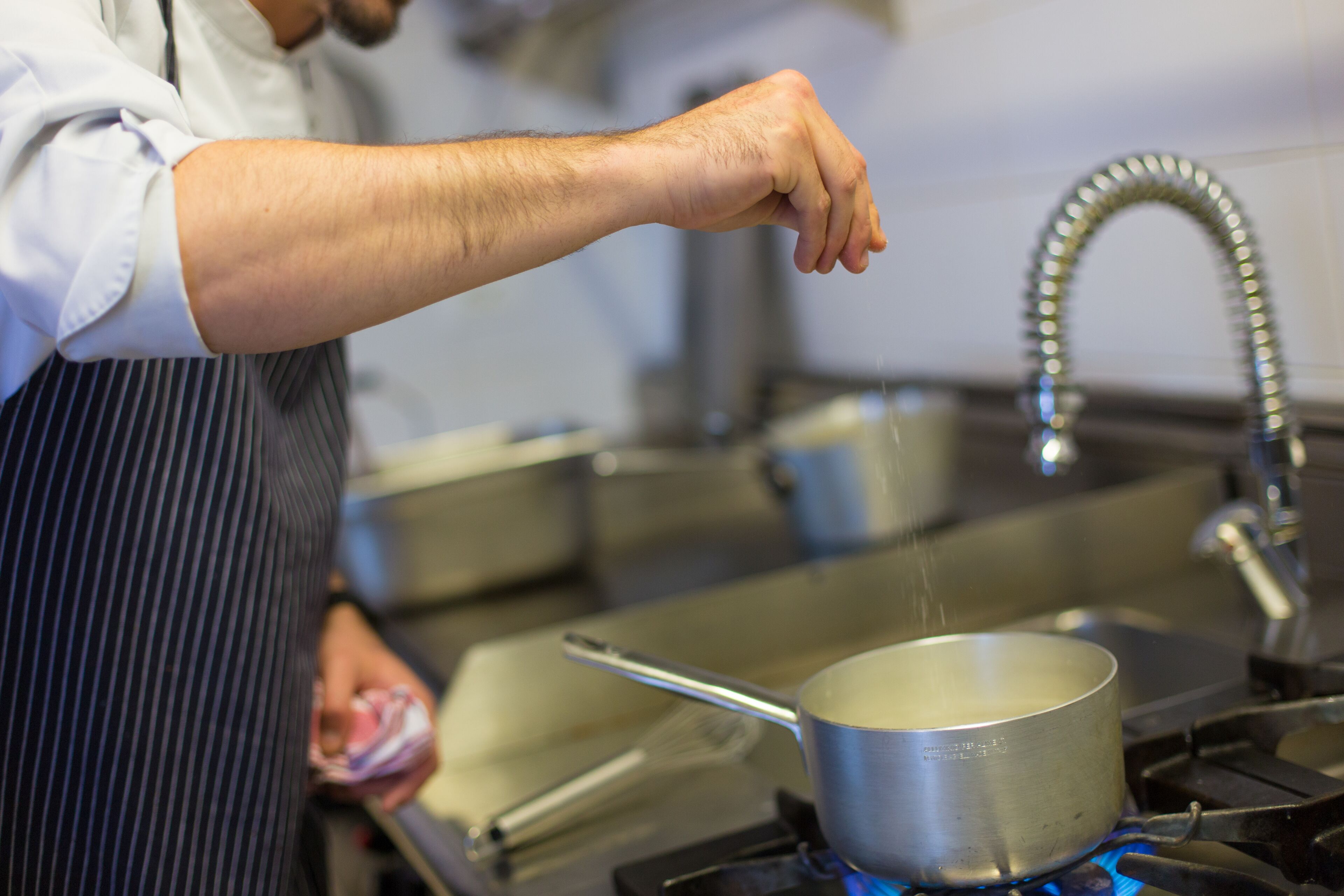 A person cooking on a stove with a pot and a pan.