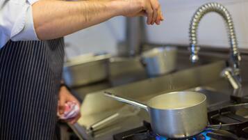 A person cooking on a stove with a pot and a pan.